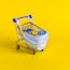 Blue shopping cart with medical mask for virus protection on yellow background. Creative concept of healthcare and safe shopping on coronavirus quarantine